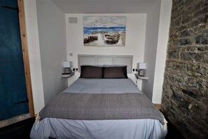Un dormitorio con una cama, un cuadro de una escena de playa, una pared de piedra y una puerta azul.