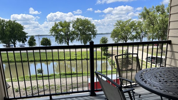 A balcony with a view of a lake, a table with chairs, and a railing. - Cozy Lake View Condo (Storm Lake)