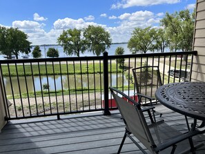 A balcony with a view of a lake, a table with chairs, and a railing. - Cozy Lake View Condo (Storm Lake)
