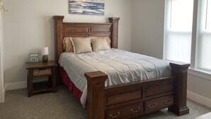 A bedroom with a wooden bed, a nightstand, a lamp, a painting on the wall, and a window with blinds. - Cozy Lake View Condo (Storm Lake)