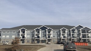 A multi-story apartment building with a grey facade, multiple balconies, and a parking area in front. - Cozy Lake View Condo (Storm Lake)