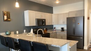 A modern kitchen with a granite countertop, stainless steel appliances, and bar stools. - Cozy Lake View Condo (Storm Lake)