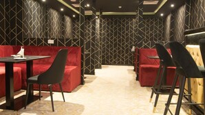 A modern interior with red upholstered seating and black chairs, geometric patterned walls, and a patterned carpet.