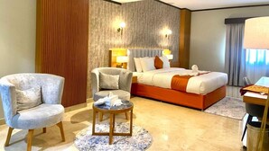 A hotel room with a large bed, two armchairs, a small round table, and a desk with a lamp.