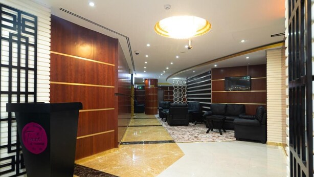 A modern lobby with a black podium, wooden paneling, a large chandelier, and a seating area with leather sofas.
