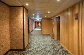 A hotel corridor with patterned carpet, wooden panel walls, and a fire hose cabinet. - Concorde Palace Hotel (Dubai)