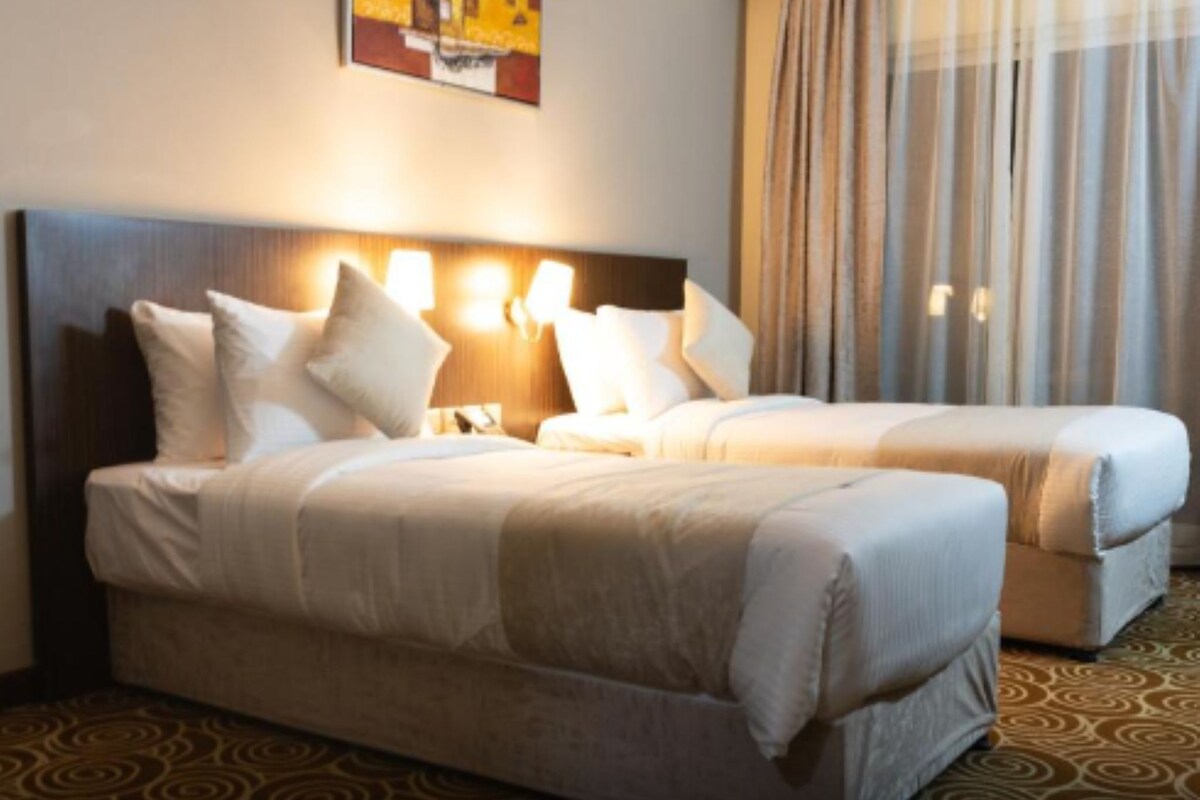 A hotel room with a large bed, two bedside tables, and a headboard with wall-mounted lights.