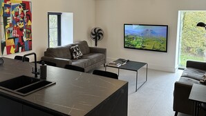 Eine moderne Küche mit einer zentralen Kochinsel, einem Essbereich mit Sofa und Couchtisch sowie einem großen an der Wand befestigten Fernseher.