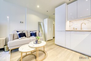 A modern living room with a sofa, a coffee table, and a kitchen area with white cabinets and a marble countertop.
