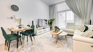 A modern living room with a dining area, a sofa, a TV, and a large window with curtains. - Urban 1BR at Binghatti Stars Dubai Silicon Oasis by Deluxe Holiday Homes (Dubai)