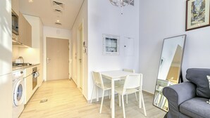 Un espace de vie compact comprenant un coin cuisine, un coin repas avec une table et des chaises, un canapé et un grand miroir.