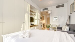 Une chambre d’hôtel moderne avec un grand lit, un canapé, un coin repas et une cuisine à l’arrière-plan.