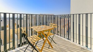 Un balcon avec une table et des chaises en bois, donnant sur un paysage urbain avec de hauts immeubles.