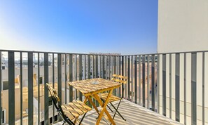 En balkon med et træbord og stole, udsigt over en by med høje bygninger.