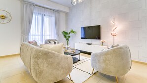 Una sala de estar moderna con un sofá, dos sillones, una mesita de centro, un televisor y una planta decorativa.