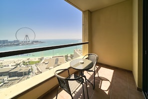 Un balcon avec une table et des chaises, donnant sur une plage et une grande roue.