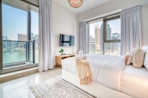 A modern hotel room with a large bed, a TV, and a view of a cityscape through large windows.