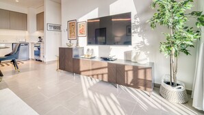 A modern kitchen with a large flat-screen TV, a dining area with a blue chair, and a potted plant. - Graceful 1BR at Park Heights Dubai Hills MBR City by Deluxe Holiday Homes (Dubai)