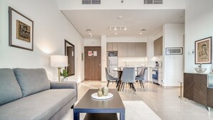 A modern living room with a grey sofa, a coffee table, and a dining area with chairs and a table. - Graceful 1BR at Park Heights Dubai Hills MBR City by Deluxe Holiday Homes (Dubai)