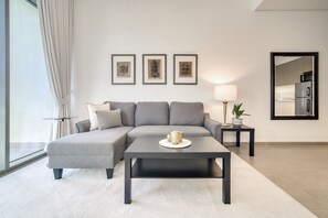 Uma sala de estar moderna com um sofá modular cinza, uma mesa de centro escura e uma pequena mesa lateral com uma luminária e uma planta. Três obras de arte emolduradas estão expostas na parede acima do sofá.