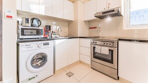 Uma cozinha moderna com armários brancos, máquina de lavar, micro-ondas, fogão e cafeteira.