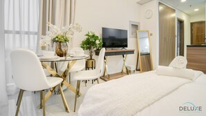 Ein Hotelzimmer mit einem Bett, einem Schreibtisch mit Fernseher, einem Esstisch mit Stühlen und einer Topfpflanze.