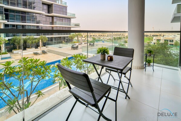 Un balcon avec une piscine, deux chaises, une table et une plante en pot.