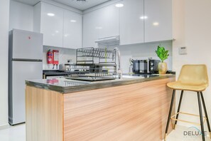 A modern kitchen with white cabinets, a stainless steel refrigerator, a built-in oven, a coffee machine, and a small island with a sink.