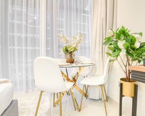 A modern dining area with a round glass table, white chairs, and a potted plant.
