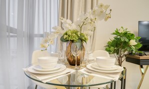 A dining table set with white plates, bowls, and a vase of white orchids.