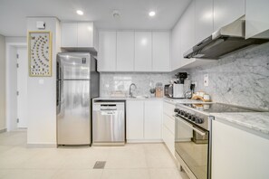 A modern kitchen with stainless steel appliances, white cabinetry, and a marble backsplash.