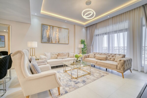 A spacious living room with a large sofa set, a glass coffee table, and a modern chandelier.