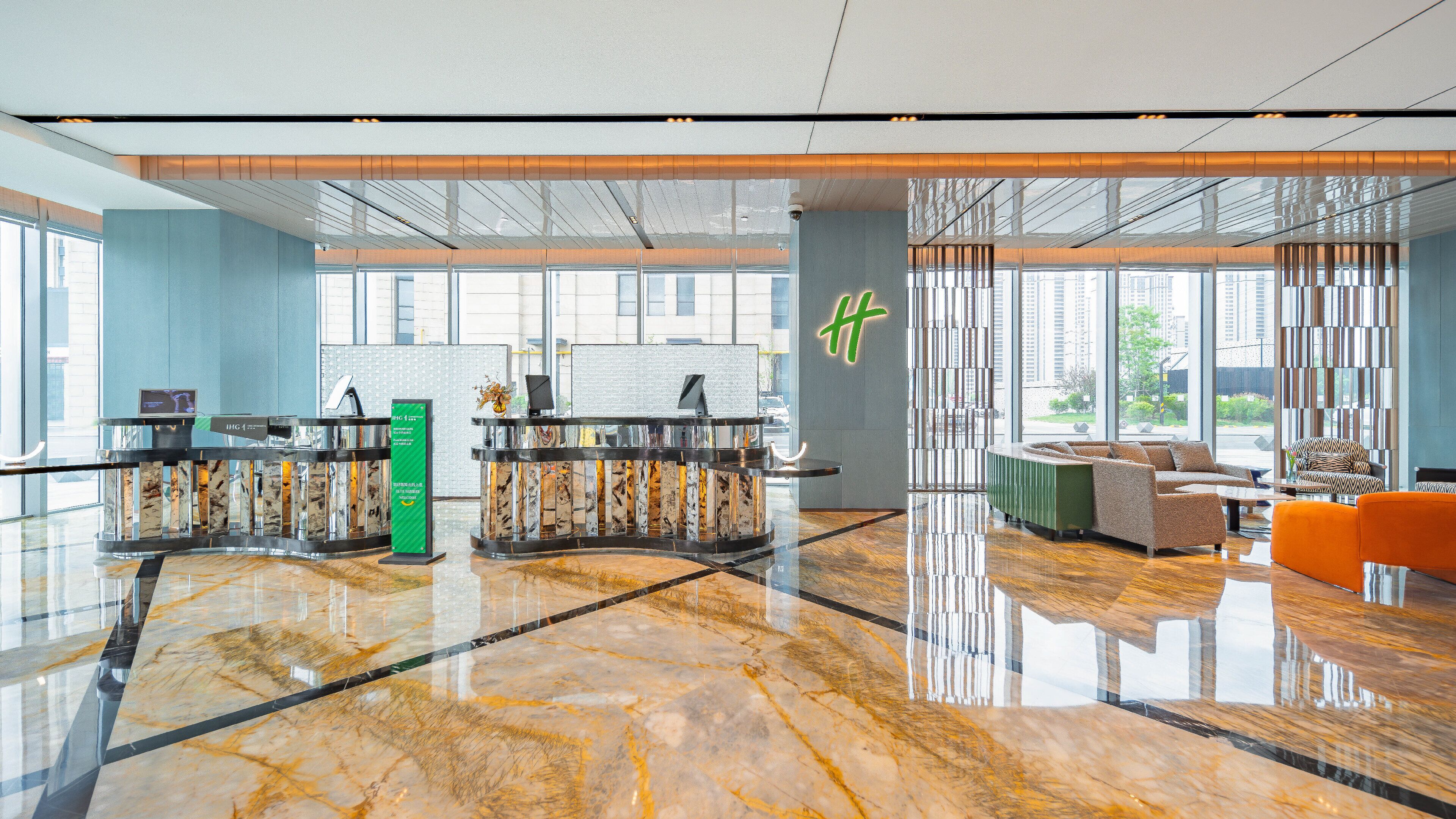 A modern hotel lobby with a marble floor, reception desks, seating area, and large windows offering city views.