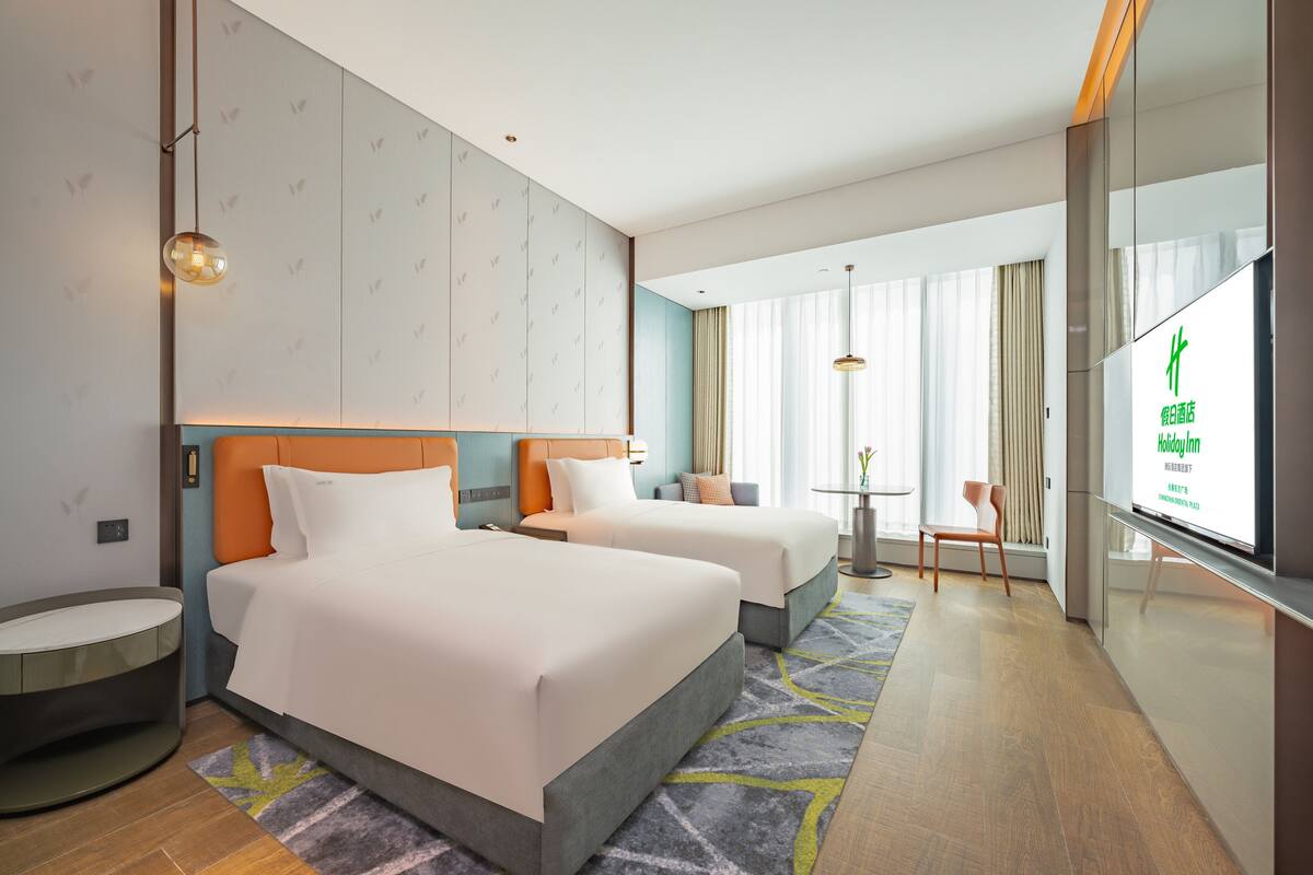Een hotelkamer met twee bedden, een tafeltje, een stoel en een televisie.
