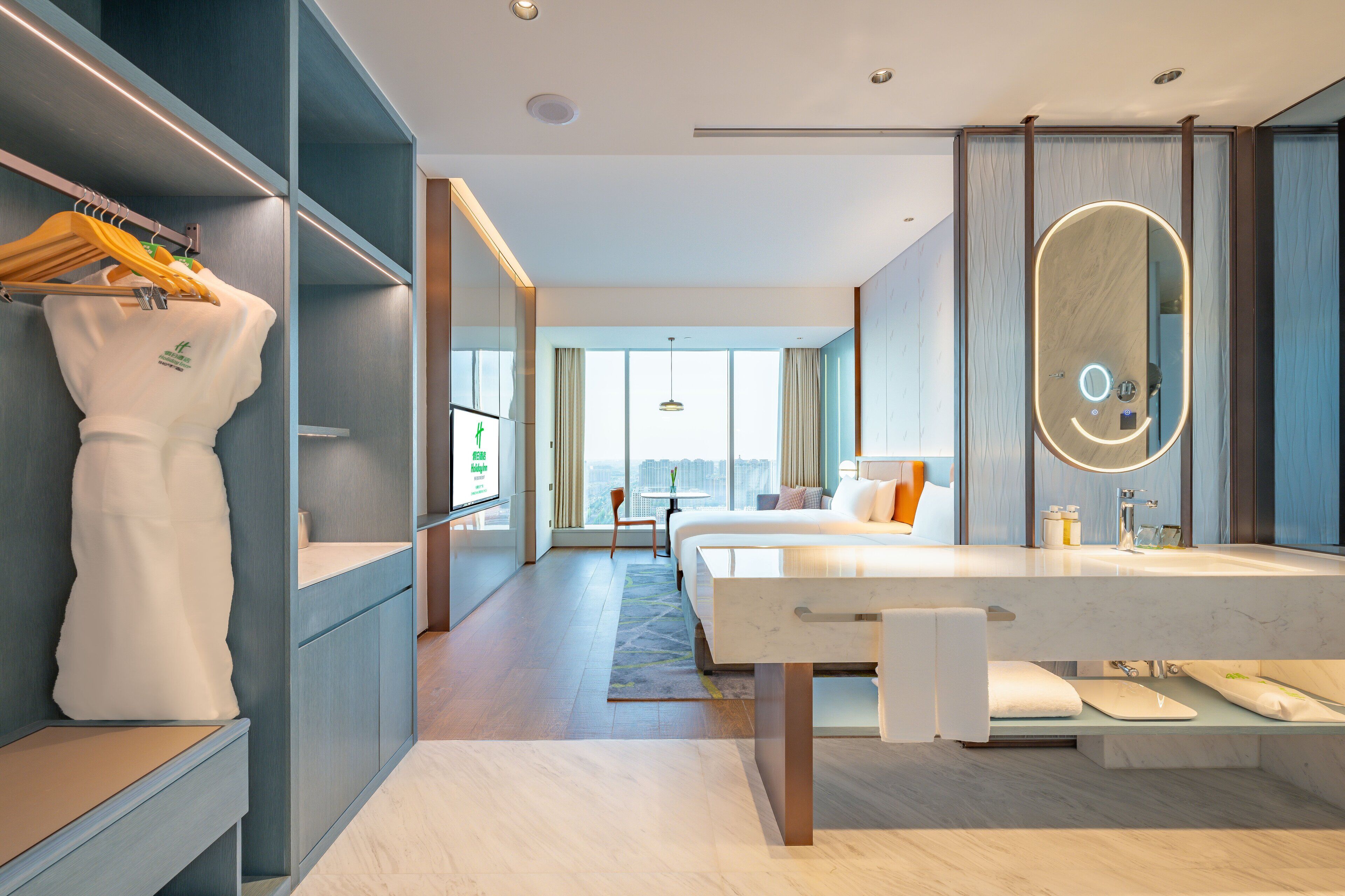 A modern hotel room with a large bed, a bathroom with a large mirror, and a view of the city.