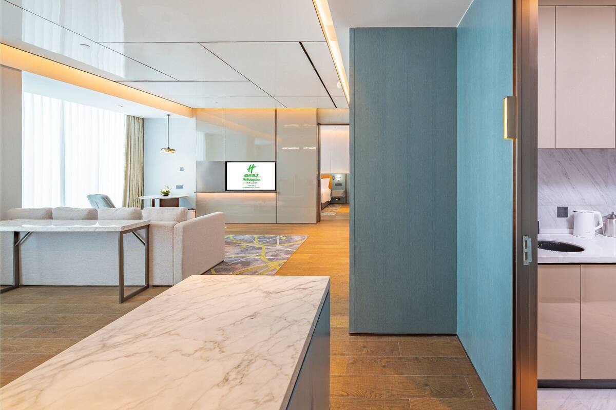 Een moderne hotellobby met een receptiebalie, een zithoek en een televisiescherm waarop de naam van het hotel staat.