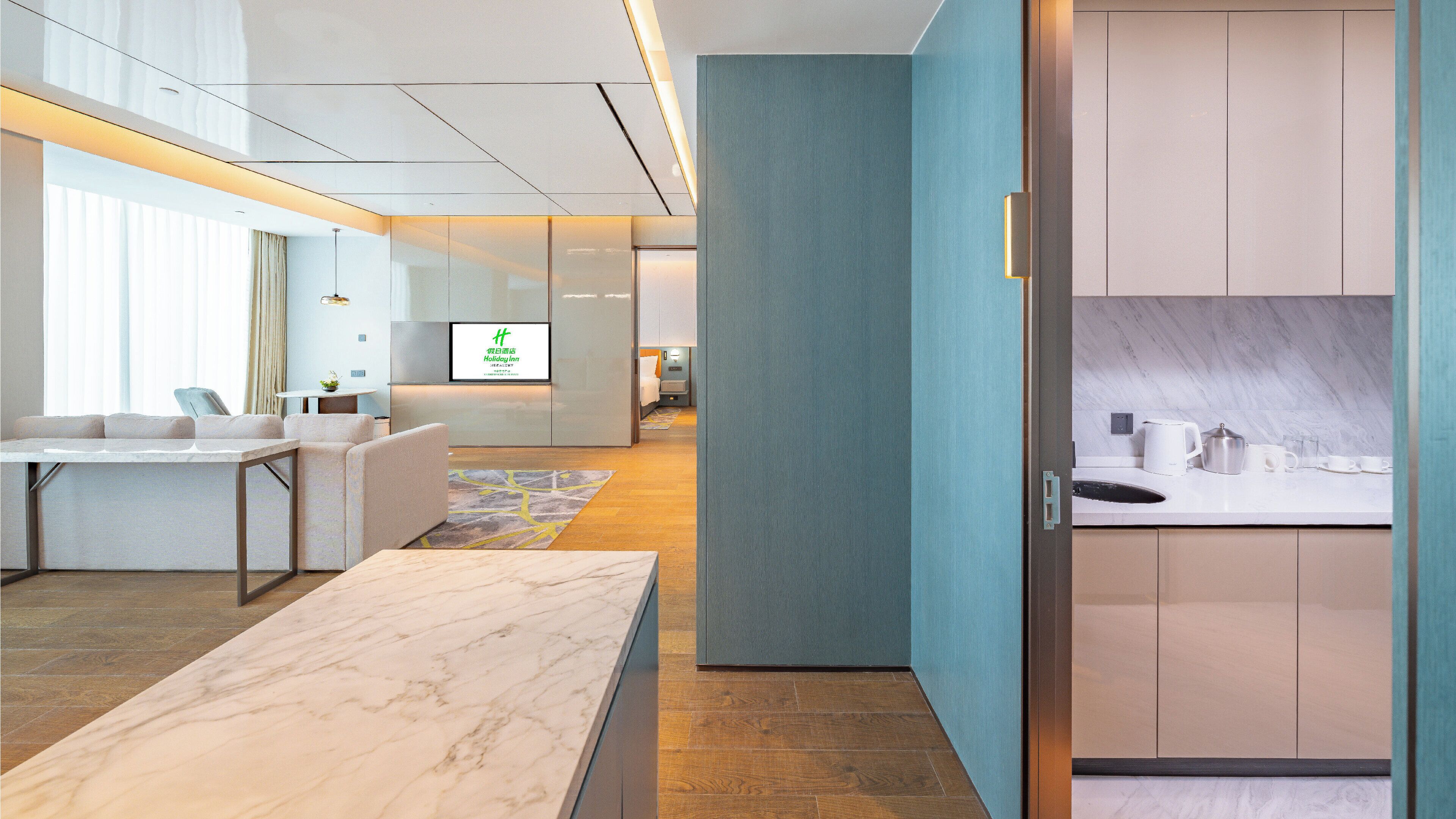 A modern hotel lobby with a reception desk, seating area, and a visible television screen.