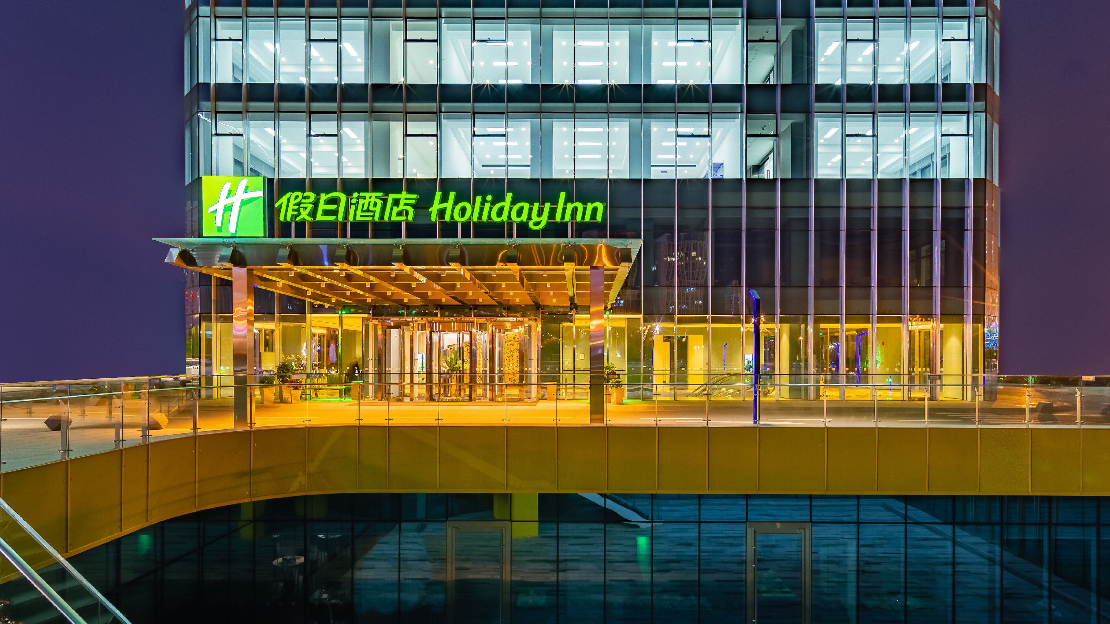 Un hotel Holiday Inn con fachada de vidrio moderna y un área de entrada cubierta.