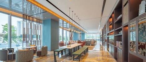 A modern hotel lobby with a marble floor, seating areas, and large windows offering views of the city.