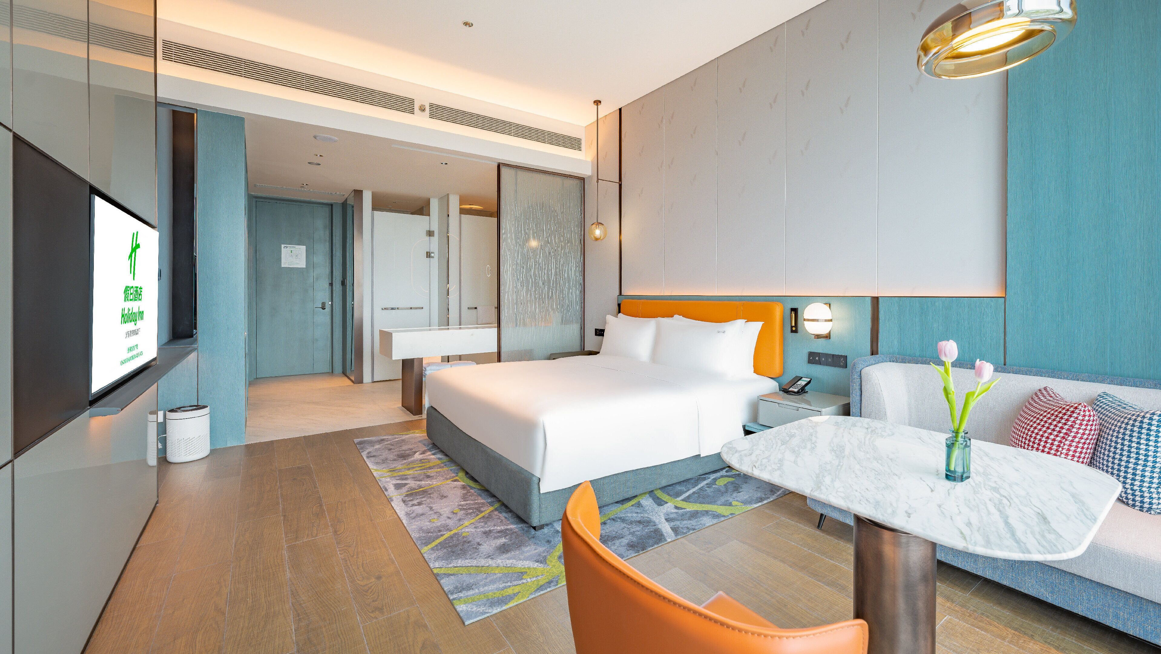 A modern hotel room with a large bed, a desk, a chair, and a TV.
