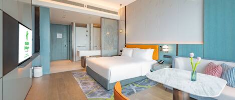 A modern hotel room with a large bed, a desk, a chair, and a TV.