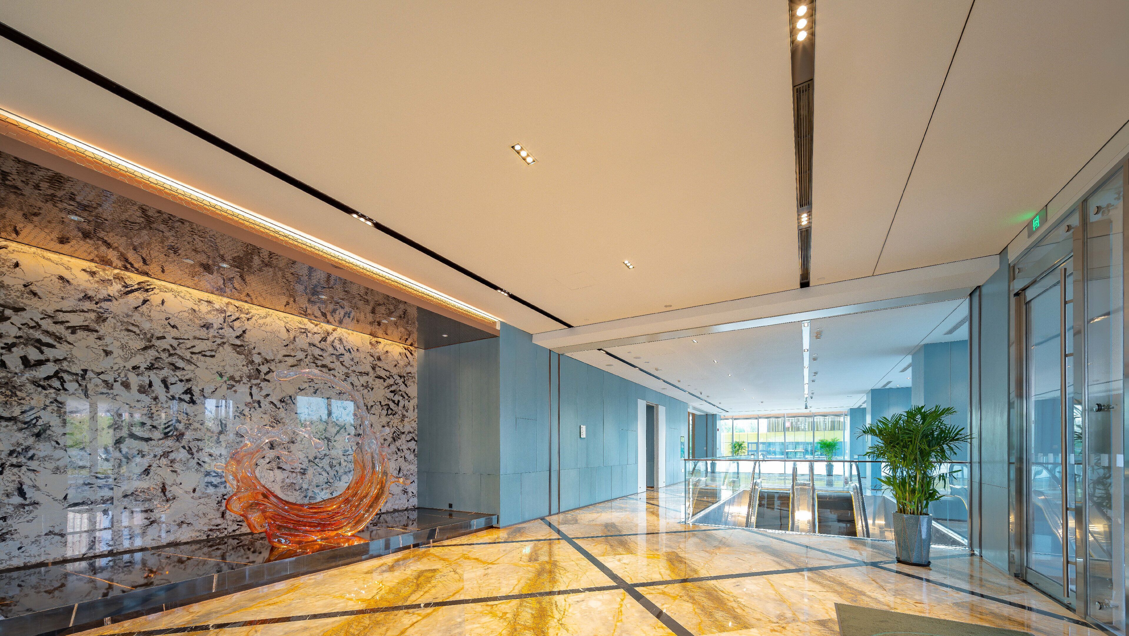 Een moderne lobby met een marmeren vloer, een glazen lift en een grote glazen wand.