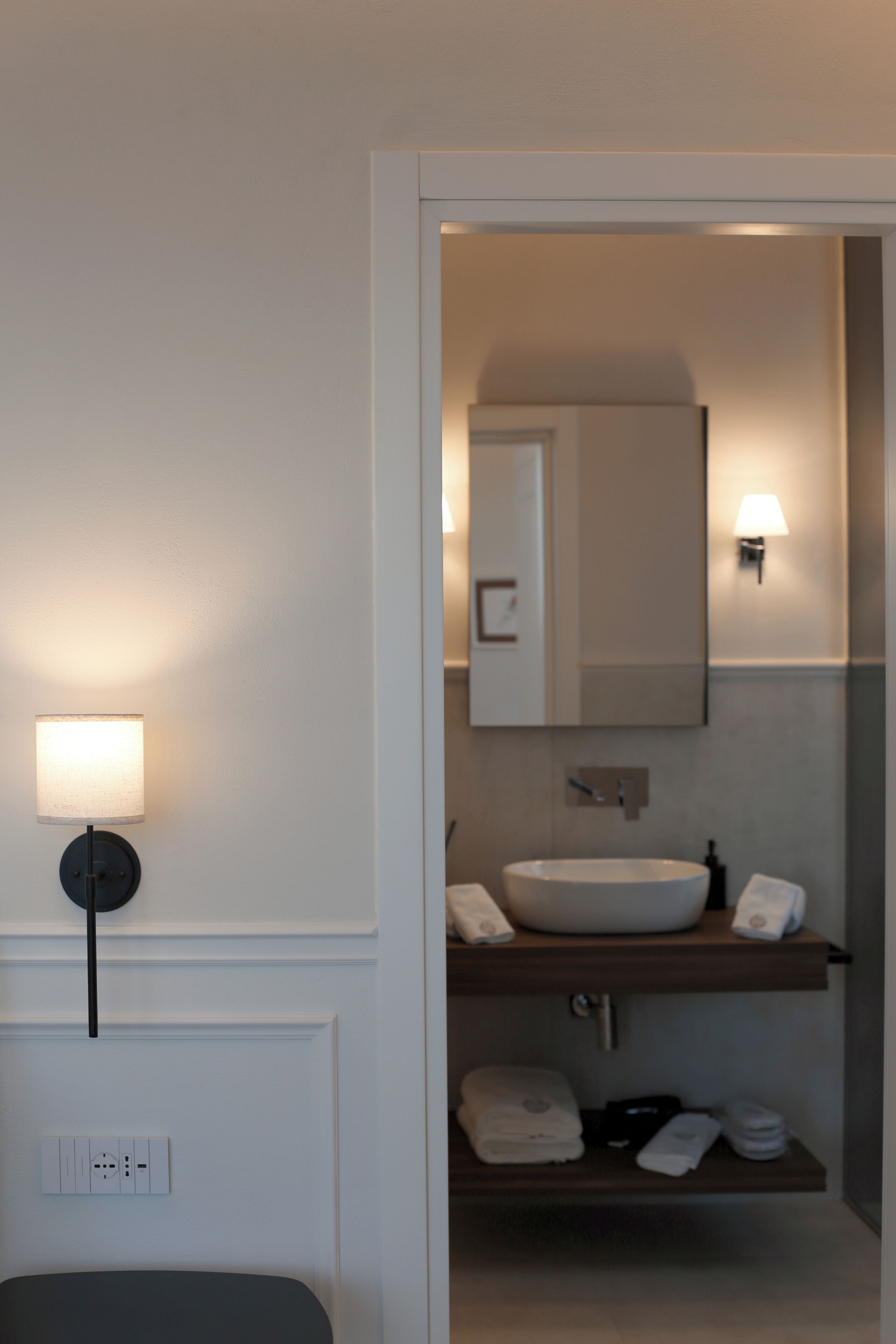 A modern bathroom with a white sink, a mirror, and a wall-mounted light fixture.