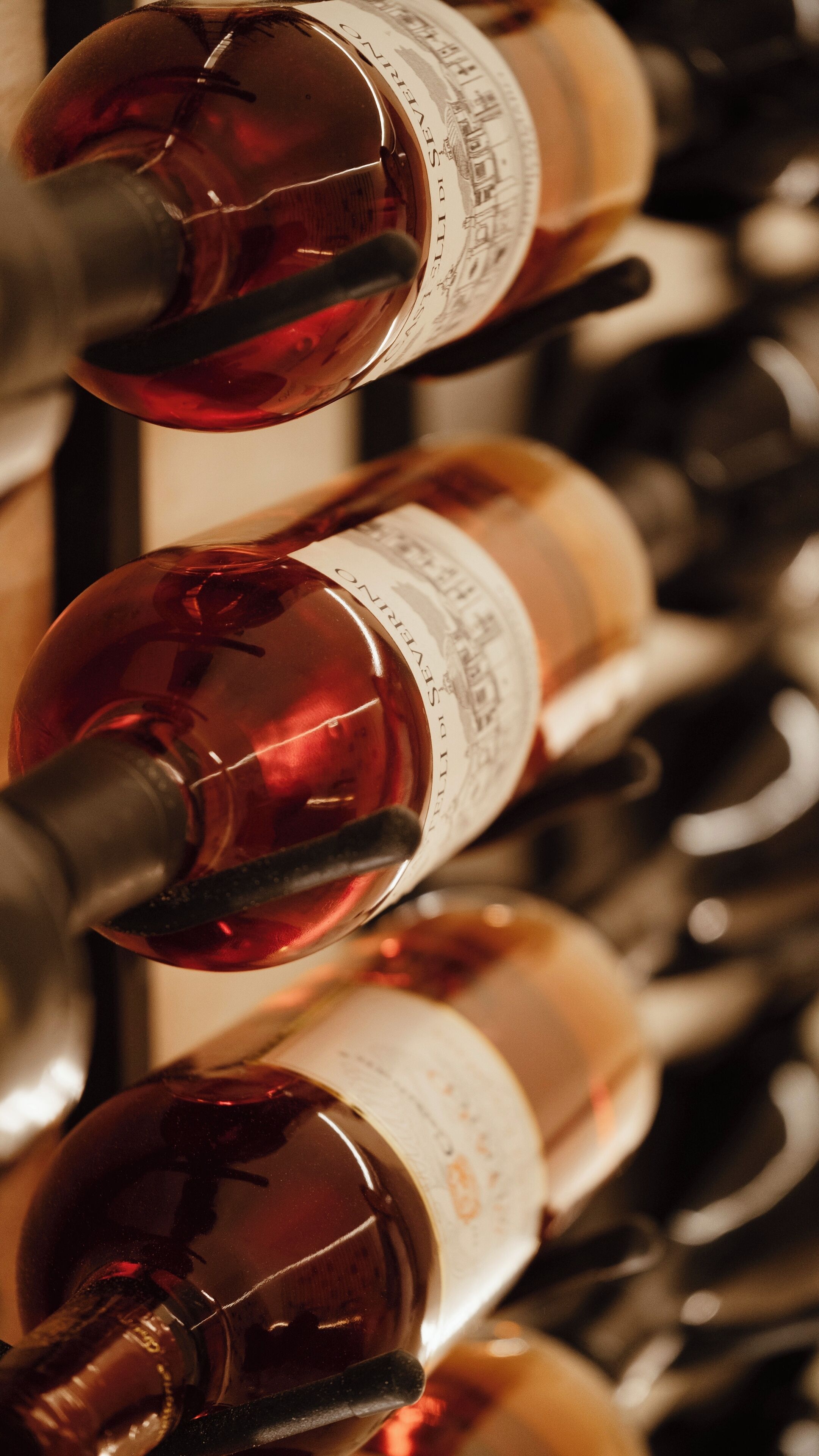 A row of wine bottles with labels, some with corks, in a dimly lit setting.