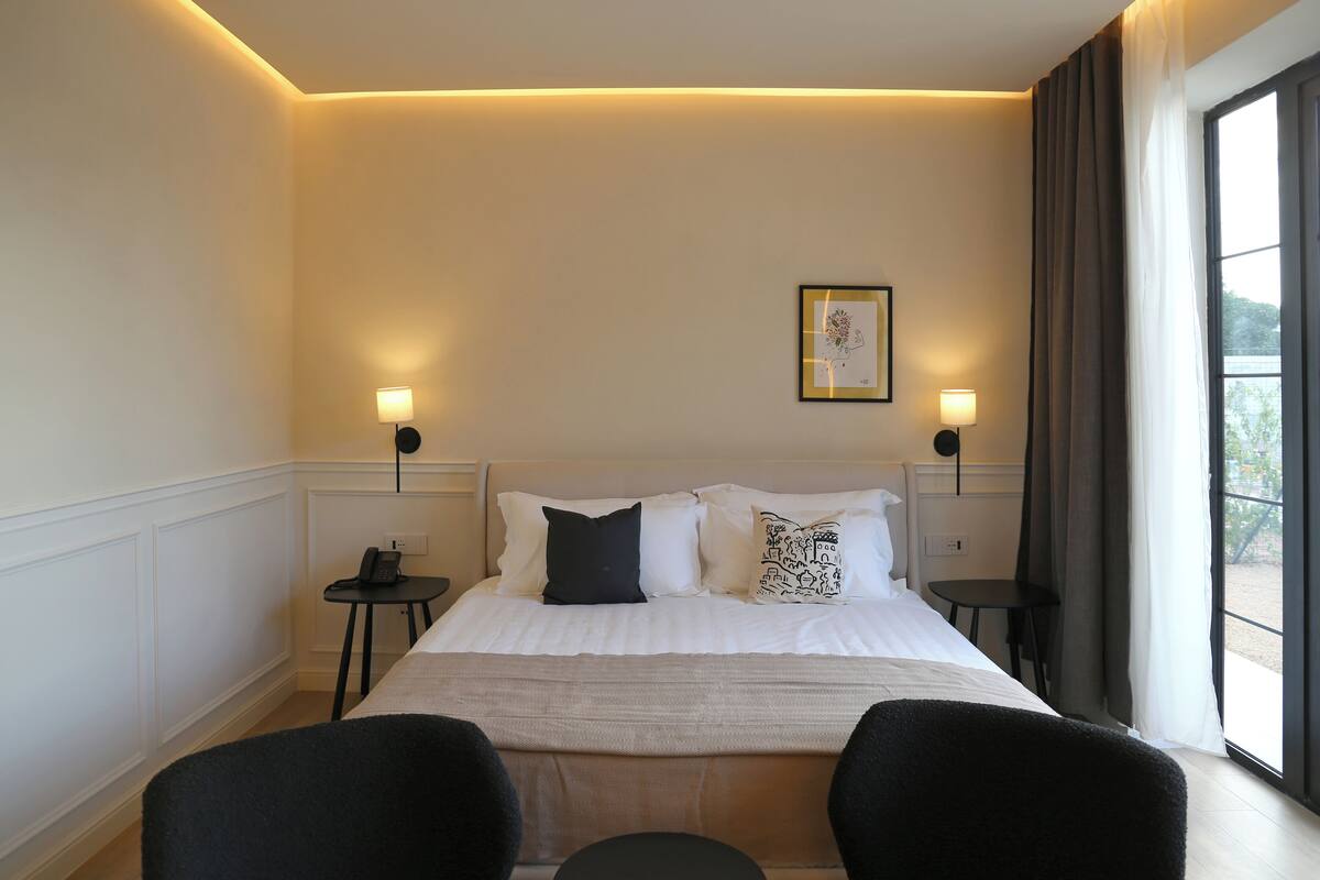 A hotel room with a large bed, two bedside tables, a small table, and a chair.
