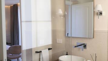 Un baño moderno con mampara de vidrio, tocador de madera, un espejo grande y lavabo blanco.