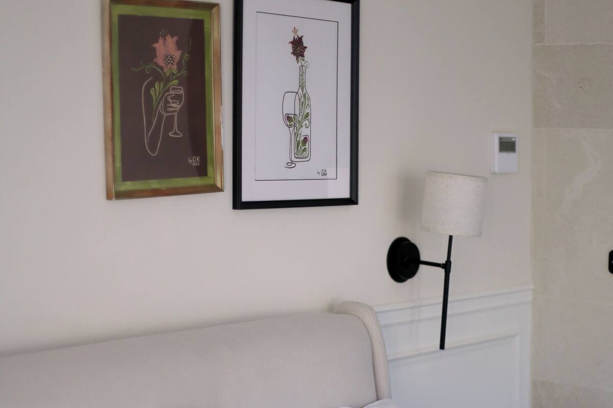 A bedroom with a bed, white bedding, a black pillow, and two framed artworks on the wall.