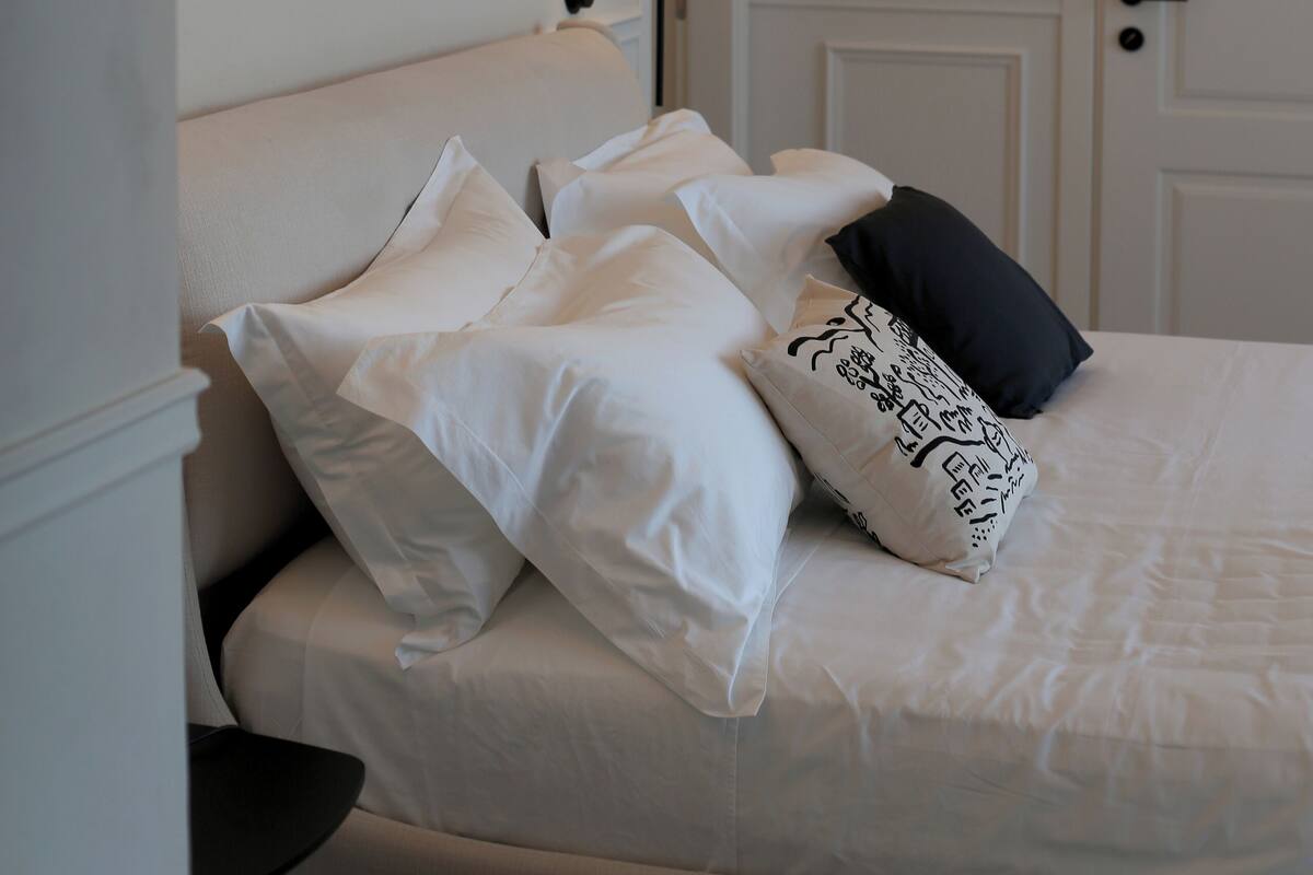 A neatly made bed with white and black pillows, a bedside lamp, and a framed picture on the wall.