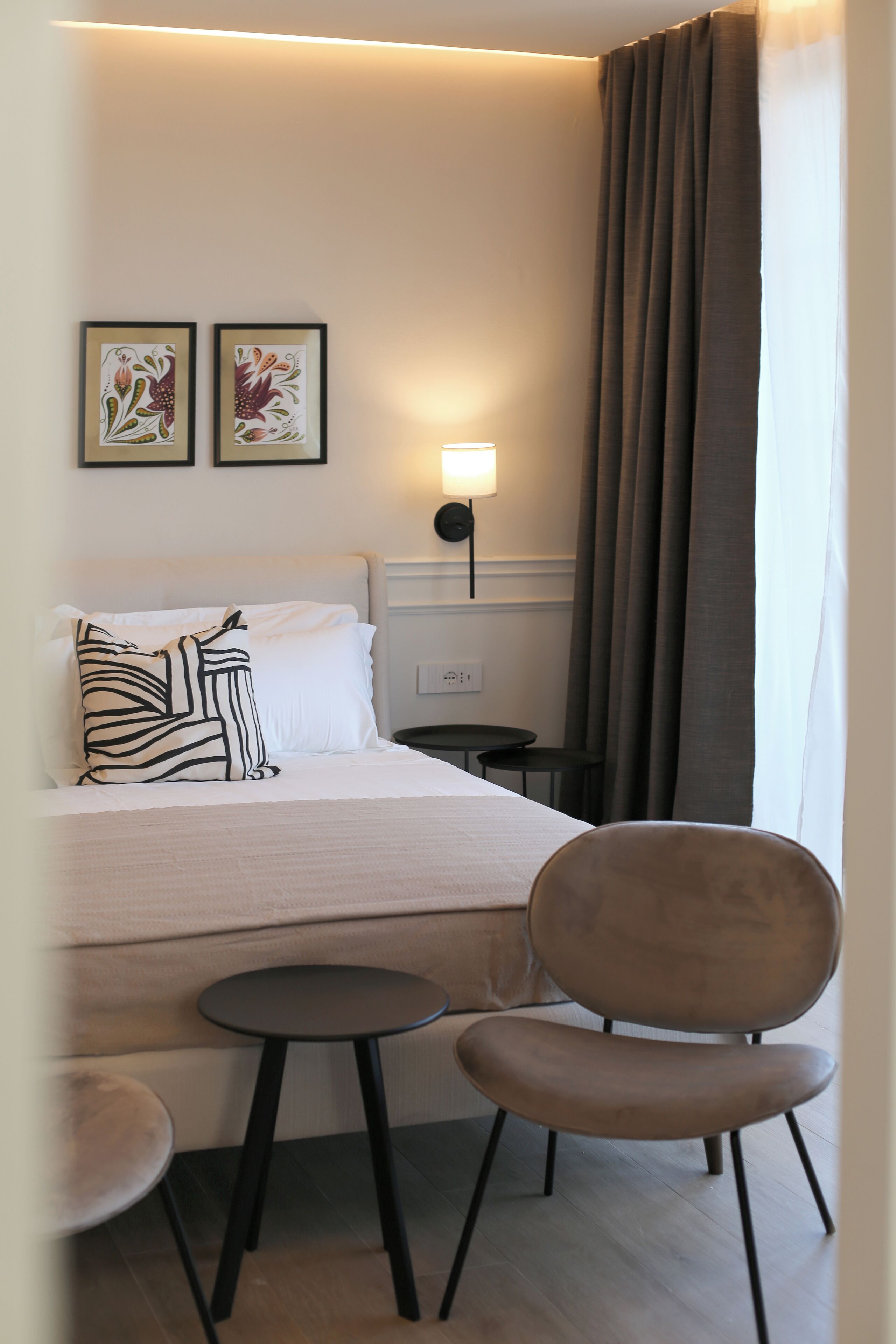 Une chambre d’hôtel comprenant un lit, deux oreillers, une table de chevet, une chaise et une lampe fixée au mur.