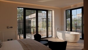 A modern hotel room with a large bed, a black chair, a round table, and a large bathtub. - Salento Winery Lodge (Manduria)